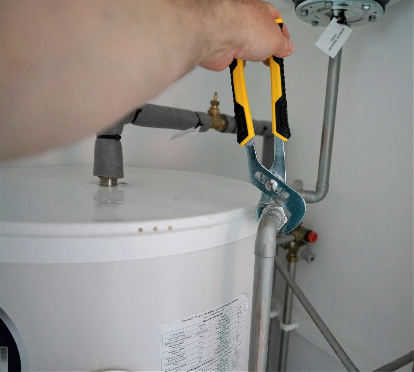 Installer with pliers on a hot water tank connection